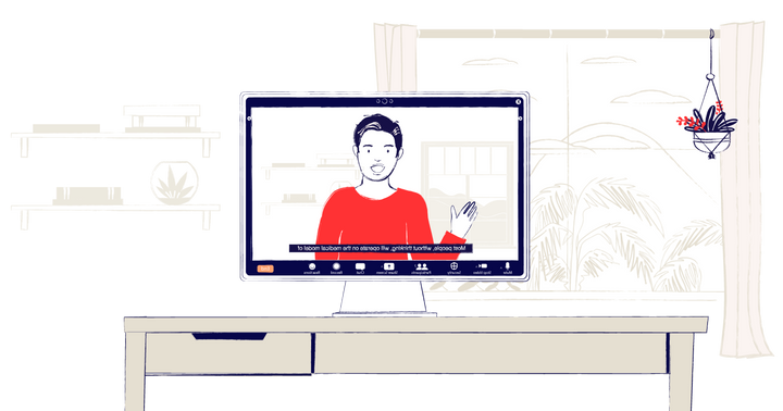 A computer screen on a desk showing a webinar. A man wearing a read sweater is speaking, with live captions.